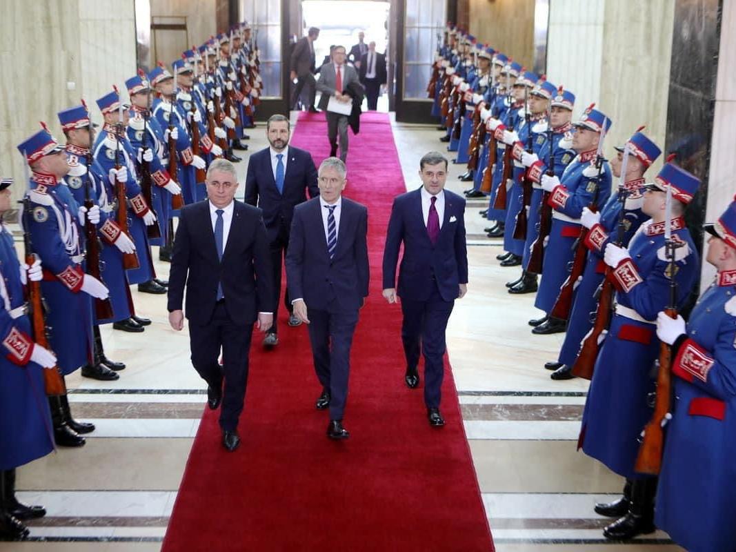 El Ministro del Interior, Fernando Grande-Marlaska, con el Ministro del Interior de Rumania entrando por una alfombra en un edificio, ambos lados guardia
