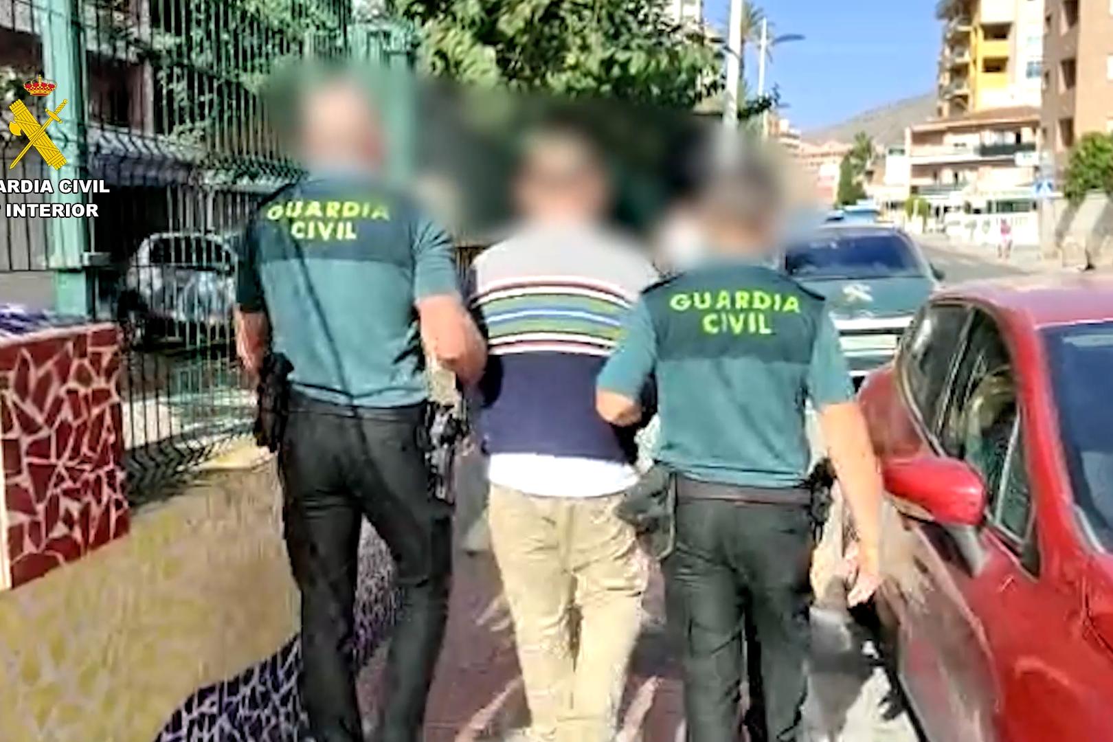 Dos agentes de la guardia civil trasladan a uno de los detenidos en la operación