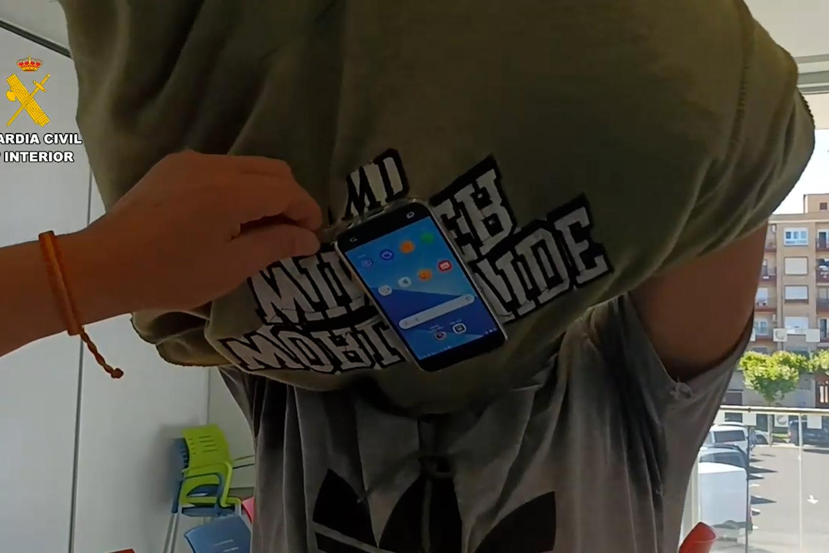 Imagen de uno de los detenidos donde se ve el móvil que ocultaba bajo la ropa para obtener de manera fraudulenta la autorización para conducir vehículos a motor