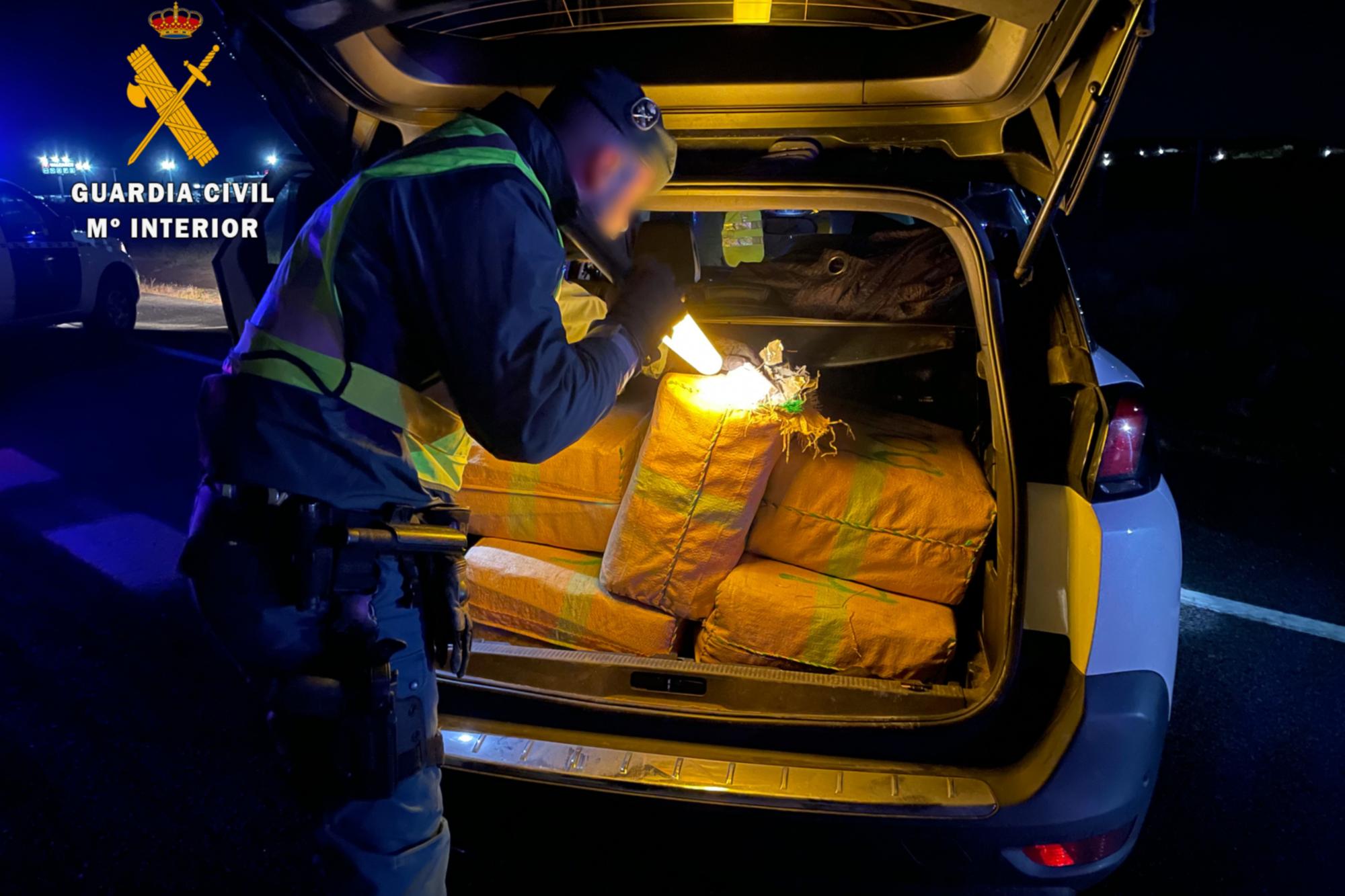 Un guardia civil con una linterna mira los fardos de hachis en el maletero de un coche